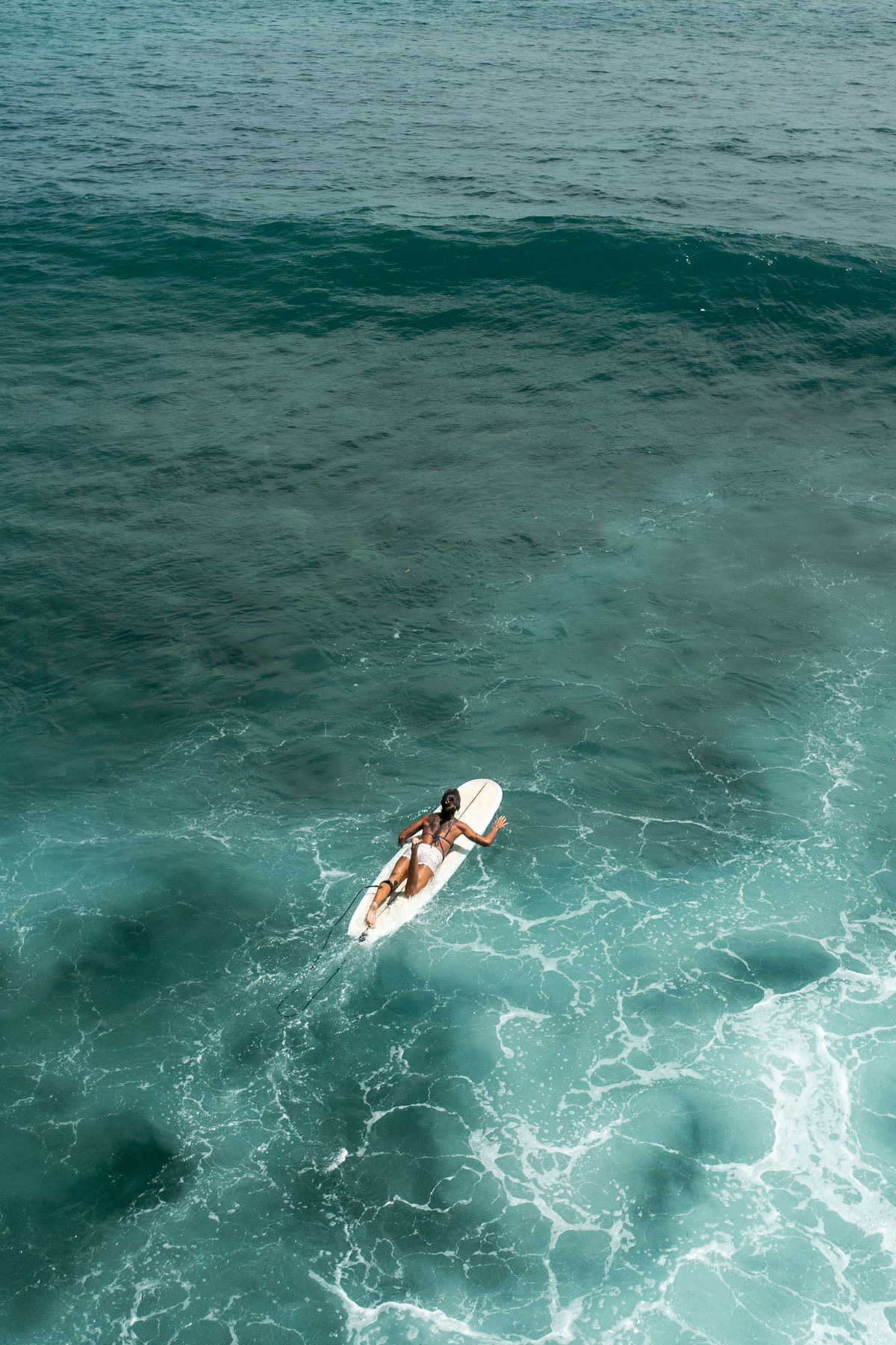 Aerial view of a lone surfer paddling across open ocean water