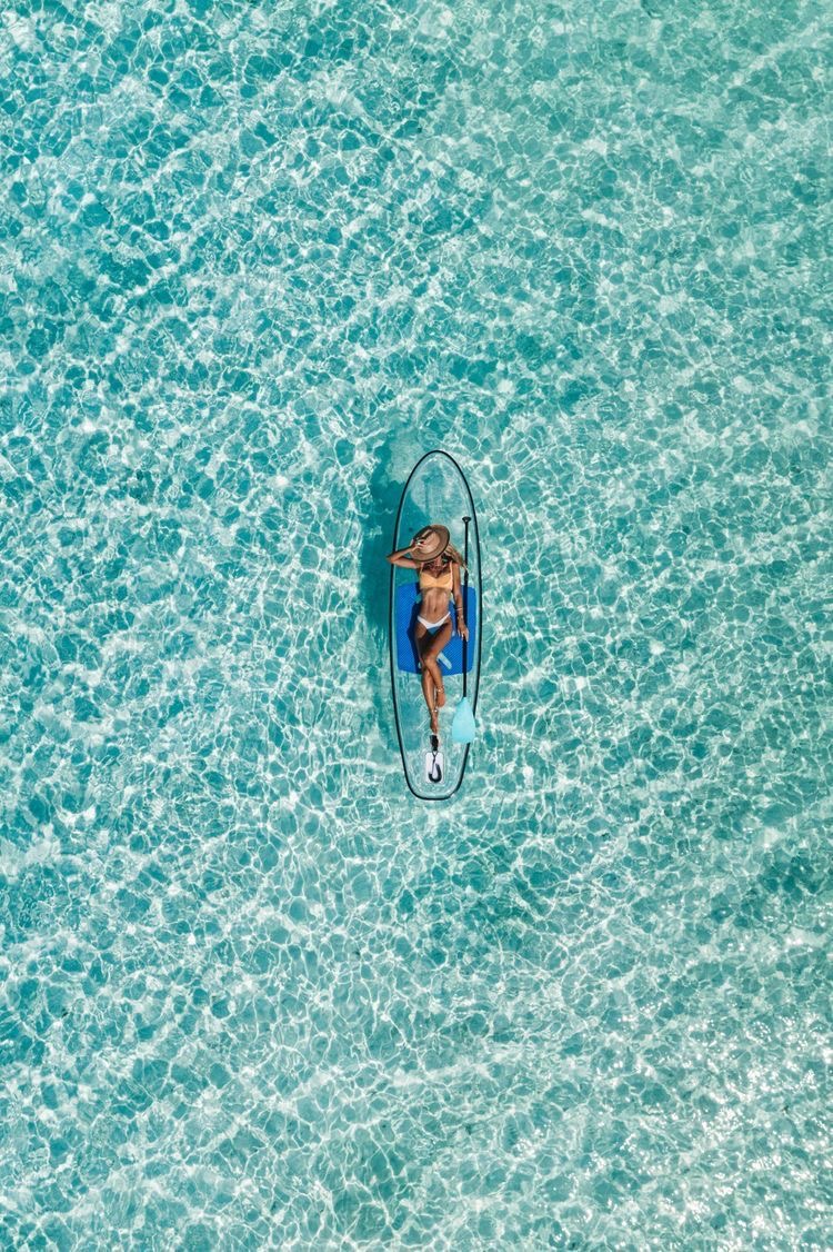 Aerial view of a woman resting on a paddleboard in clear turquoise water